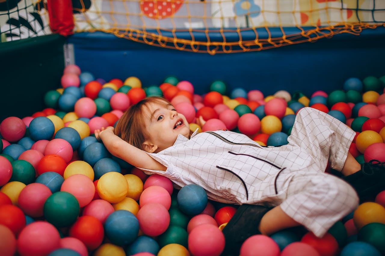 services-04 A joyful child playing in a vibrant ball pit full of colorful balls, indoors.