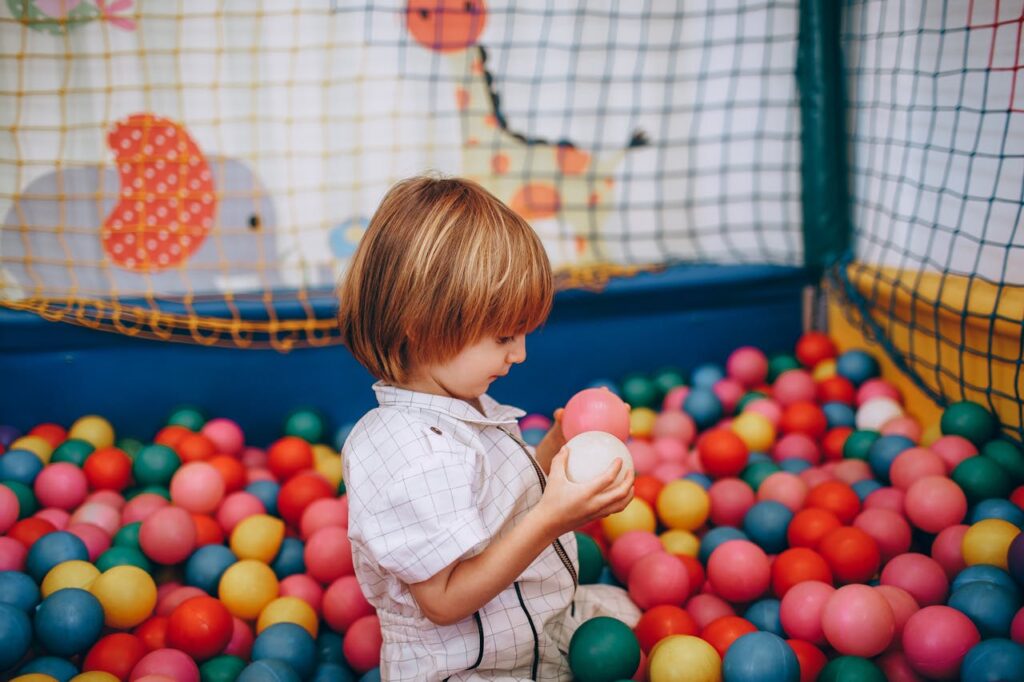 Cute child enjoying a colorful ball pit at an indoor play area, surrounded by vibrant colors.