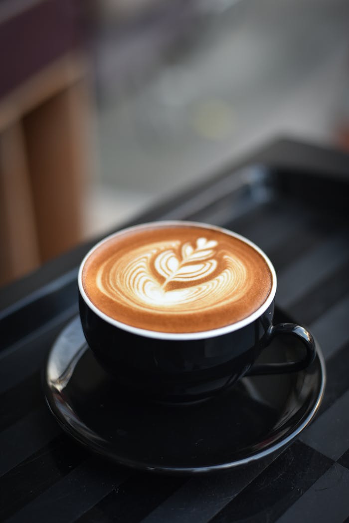 why-choose-us A beautifully crafted cappuccino with intricate latte art in a black ceramic mug on a dark surface.
