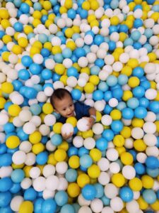 A happy baby playing in a vibrant ball pit, surrounded by colorful balls in Indonesia.