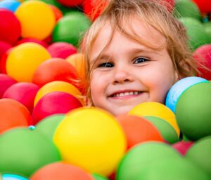 Smiling child having fun in a colorful ball pit, showcasing happiness and playtime.