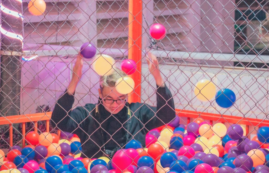 A joyful adult in a colorful ball pit surrounded by a lively atmosphere.