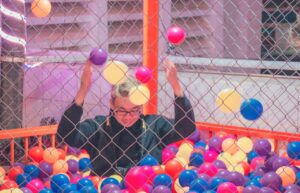 A joyful adult in a colorful ball pit surrounded by a lively atmosphere.